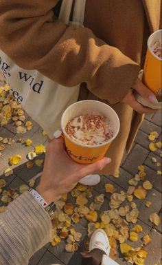 two people are holding drinks in their hands and looking at the ground with fallen leaves on it