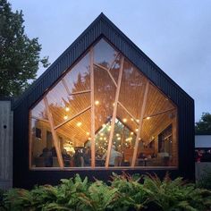 a black building with lots of windows and plants in front of it at night time