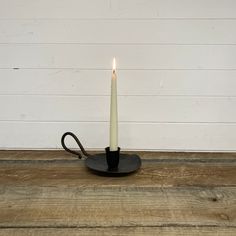 a lit candle sitting on top of a wooden floor next to a white brick wall