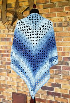 a blue crocheted shawl hanging on a brick wall