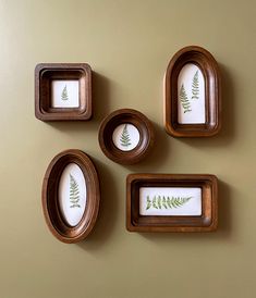 three wooden frames with green leaves on them hanging on a wall next to two framed pictures