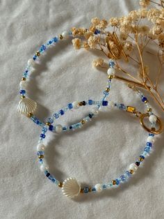 two bracelets with beads and seashells are on a white sheet next to dried flowers