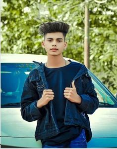 a young man standing in front of a blue car with his hands on his hips