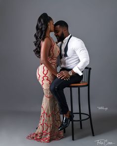 a man and woman are sitting on a chair kissing in front of a gray background