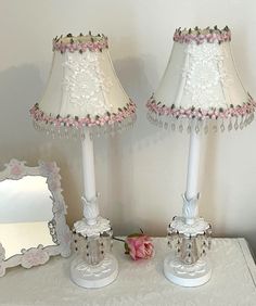 two white lamps with pink flowers on them sitting on a table next to a mirror