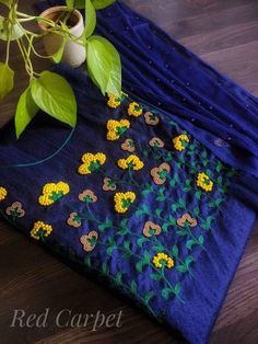 a blue cloth with yellow flowers and green leaves on it next to a potted plant