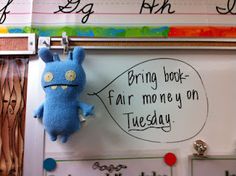 a blue stuffed animal hanging from a hook on a bulletin board with writing underneath it