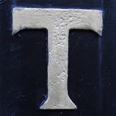 the letter t is painted white on a black background and it appears to be made out of cement