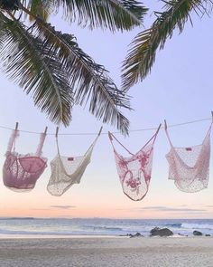 three hammocks hanging from a rope on the beach with palm trees in the background