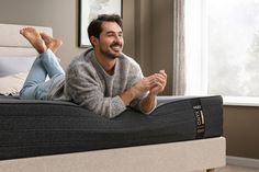 a man laying on top of a bed with his feet up in the air and smiling