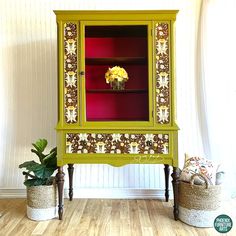 a green cabinet sitting on top of a wooden floor next to two potted plants