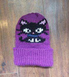 a purple knitted hat with black and white cats on it sitting on top of a wooden floor