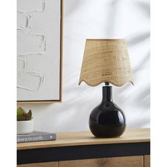 a black lamp on a table next to a white wall and a framed photograph in the background