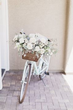 a bicycle with flowers in the basket is parked on a brick walkway near a building