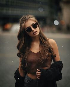 a woman with long hair and sunglasses standing in the street