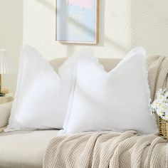 two white pillows sitting on top of a couch next to a basket filled with flowers