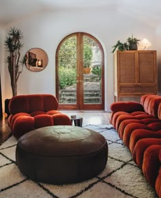 a living room filled with red couches and a round ottoman on top of a rug