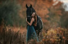 a woman in a blue dress standing next to a black horse