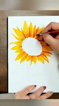 a woman is drawing a sunflower on a piece of paper