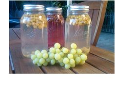 three jars filled with grapes sitting on top of a wooden table