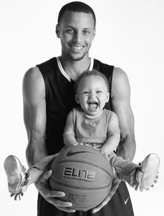 a black and white photo of a man holding a baby with a basketball in his hands