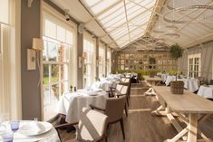 a dining room with tables and chairs covered in white tablecloths next to large windows