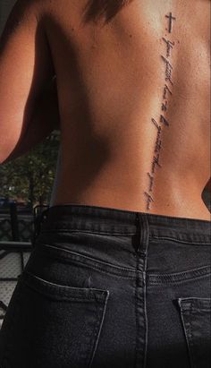 the back of a person with a cross tattoo on their left side and words written in cursive writing