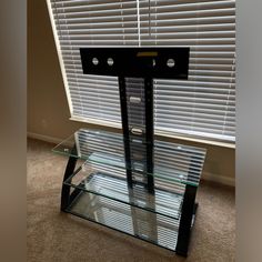 a glass table with metal legs on carpeted floor next to window covered in blinds