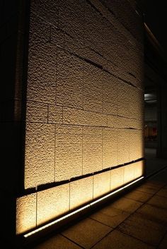 the light is shining on the side of a brick building at night, casting shadows onto the wall