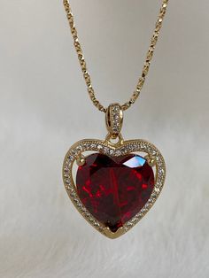 The Ruby Heart Necklace is enchanting! This heart necklace came straight out from a rom-com! It features a large heart-shaped cubic zirconia ruby crystal hugged in a micro pave frame and suspended on a dainty twisted box chain necklace. She takes all other ruby heart necklaces off the scene! Available in 24K gold or rhodium plating over steel Patent plating & sealant technology to ensure durability and long lasting wear Made in Los Angeles, CA | Nickel & Lead Free Heart Necklace With Cubic Zirconia For Valentine's Day, Gold Jeweled Ruby Necklace, Luxury Red Choker For Gift, Red Heart Cut Cubic Zirconia Necklace, Gold Red Heart Necklace, Cubic Zirconia Heart Necklace With Gemstone For Valentine's Day, Elegant Ruby Necklace With Heart Charm, Ruby Heart Charm Necklace, Gold Ruby Heart Pendant Jewelry