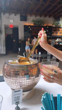 a woman holding a spoon over a bowl filled with liquid next to another person's hand