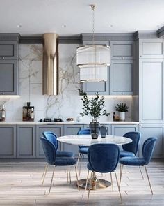 a dining room table with blue chairs and a white marble top surrounded by gray cabinets