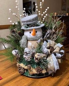 a snowman sitting on top of a table next to pine cones and evergreens