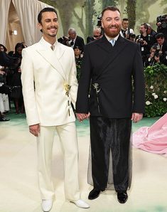 two men standing next to each other in front of photographers at a fashion show wearing suits and ties