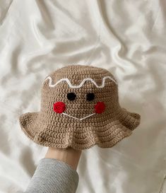 a hand is holding a crocheted brown hat with white trim and red eyes