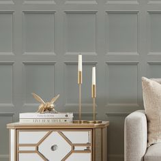 a white and gold side table with two candles on it next to a beige couch