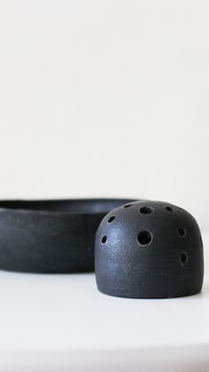 a black object sitting on top of a white table next to a bowl with holes in it