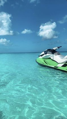 a green and white boat floating on top of clear blue water near the shore line