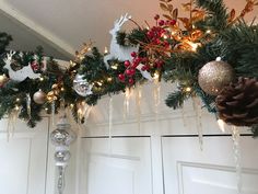 christmas decorations hanging from the ceiling in front of a white door with pine cones and red berries