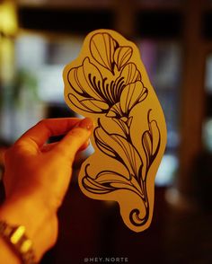 a person holding up a piece of paper that has flowers on it and leaves drawn on it