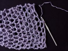 a crocheted square with a knitting needle next to it on a black surface