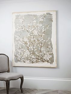 a chair sitting in front of a painting on the wall next to a white flowered tree