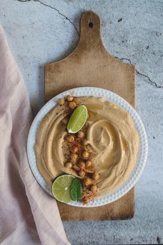 a white plate topped with hummus next to a cutting board and lime wedges