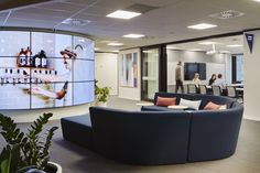 an office lobby with couches, tables and people walking around the room on large screens