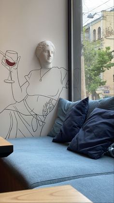 a blue couch sitting in front of a window next to a wall with a drawing on it