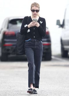 a woman in black sweater and jeans looking at her cell phone while walking down the street