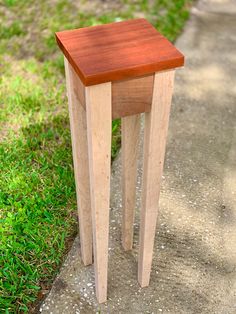 a small wooden table sitting on top of a cement ground next to grass and dirt road