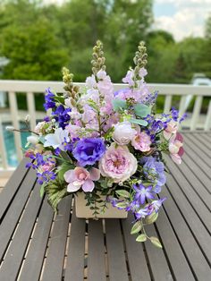 a vase filled with purple and white flowers sitting on top of a wooden table next to a pool