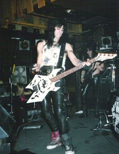 a man in black leather pants holding a white guitar and standing next to other musicians