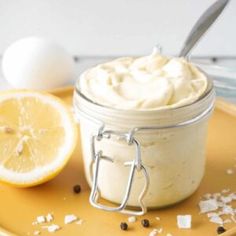 a jar filled with whipped cream next to an egg and sliced lemon on a yellow plate